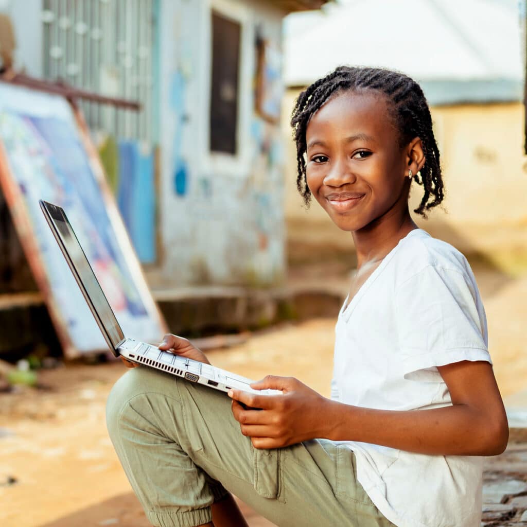 Child using a laptop in a rural African village, representing digital inclusion enabled by the MTN Satellite Trial.